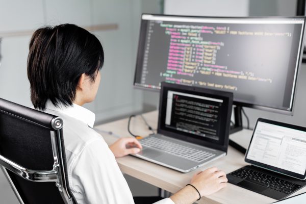 A software developer working on code with multiple screens in a modern office setting. Wallpaper 4K