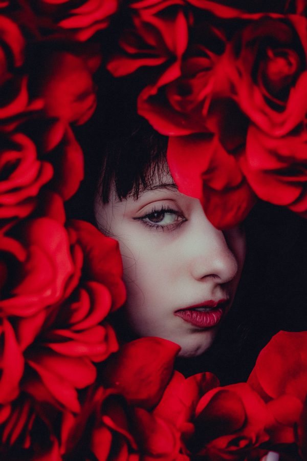 A striking close-up portrait framed with vivid red roses, highlighting beauty and mystery. Mobile 4K