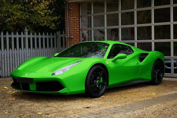 A striking green sports car parked in front of a garage with a glass facade and wooden fence. Voitures 4K