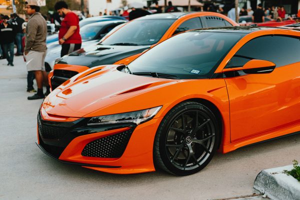 A striking orange supercar parked at an outdoor car show, drawing attention with its sleek design. Voitures 4K