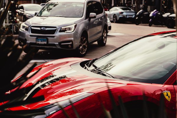 A striking red luxury sports car parked on a city street alongside other vehicles. Voitures 4K