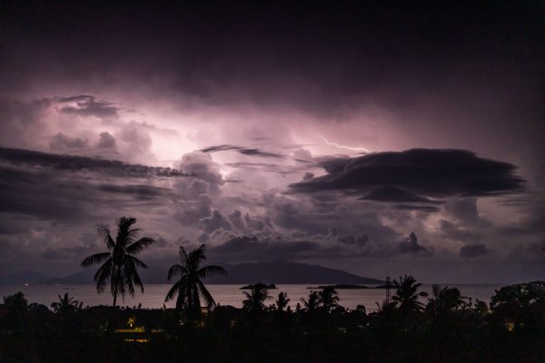 A striking view of lightning illuminating dark clouds above a tropical ocean landscape. Dark 4K