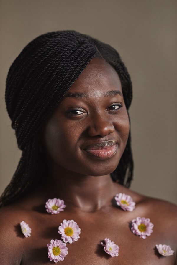 A studio portrait of a smiling woman with pink flowers on her shoulders. Mobile 4K