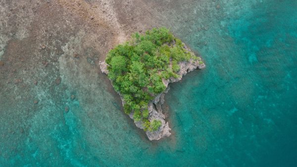 A stunning aerial view of a small, lush tropical island surrounded by the clear blue sea in the Philippines. Nature 4K
