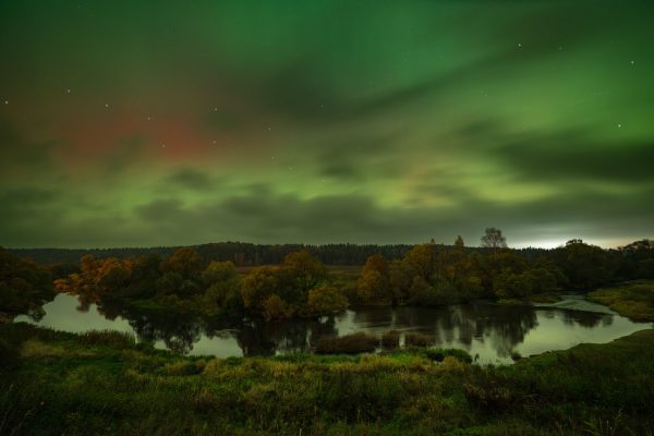 A stunning aurora borealis above a serene night landscape with a reflective river. Espace 4K