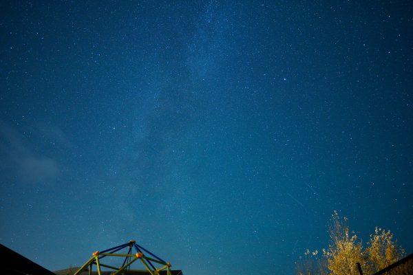 A stunning long exposure photograph capturing a star-filled night sky with subtle cloud formations and tree silhouettes. Espace 4K