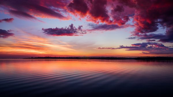 A stunning sunset paints the horizon with vibrant colors over calm ocean waters. Abstrait 4K