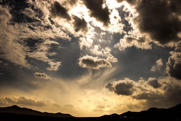 A stunning view of a cloudy sky at sunset over mountainous terrain, creating a dramatic and serene atmosphere. Dark 4K