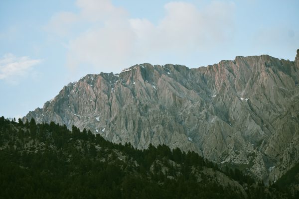 A stunning view of a rugged mountain range above a lush evergreen forest under a partly cloudy sky. Nature 4K