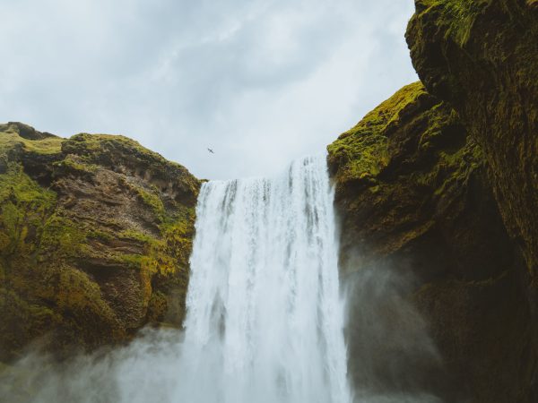 A stunning waterfall cascades between moss-covered cliffs under an overcast sky. Nature 4K