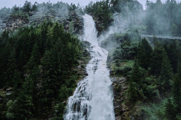 A stunning waterfall cascading down a rocky cliff surrounded by verdant trees and mist. Nature 4K