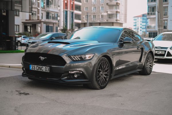 A stylish black Ford Mustang parked on a city street, showcasing its sporty design in a modern urban environment. Voitures 4K