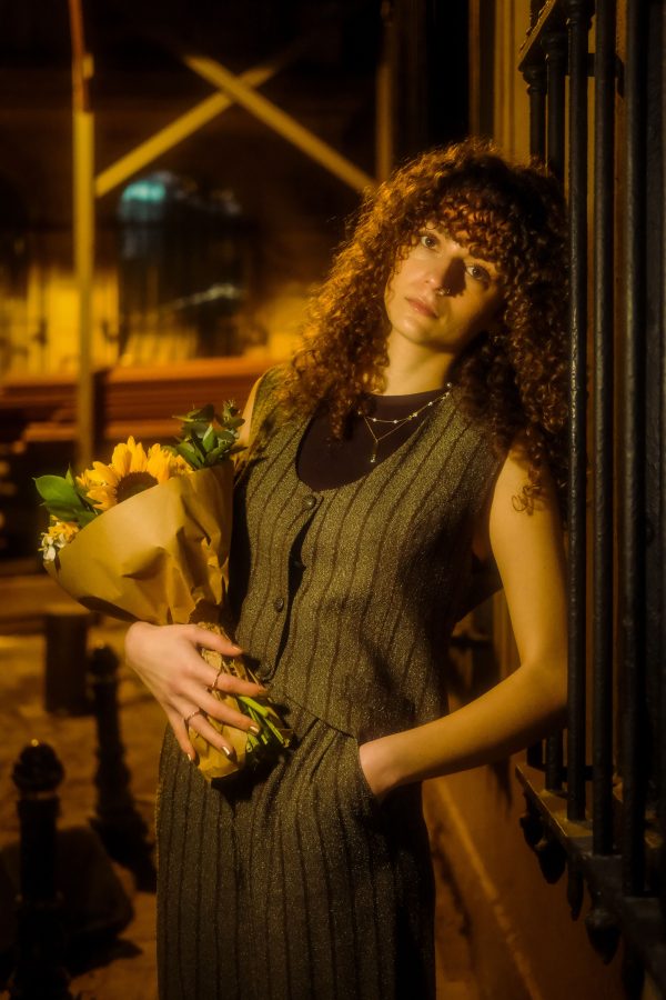 A stylish woman with curly hair holds a bouquet on an urban night street, creating a moody portrait. Mobile 4K