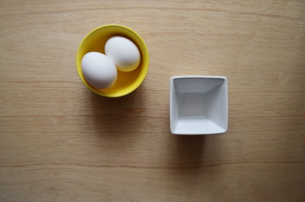 A top-down view of two white eggs in a yellow bowl on a wooden surface. Minimaliste 4K