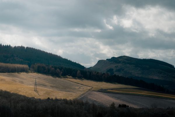 A tranquil mountain landscape with fields and cloudy sky, creating a dramatic scene. Nature 4K