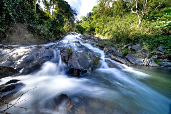 A tranquil waterfall cascading over rocks in a lush, green forest landscape. Nature 4K