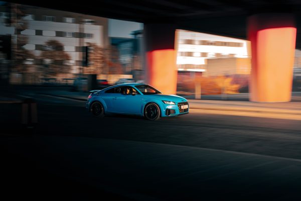 A vibrant blue car speeds through an urban Scottish cityscape at dusk, emphasizing motion and architectural elements. Voitures 4K
