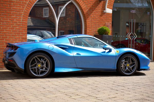 A vibrant blue Ferrari supercar is parked in an urban location, highlighting sleek design and luxury. Voitures 4K