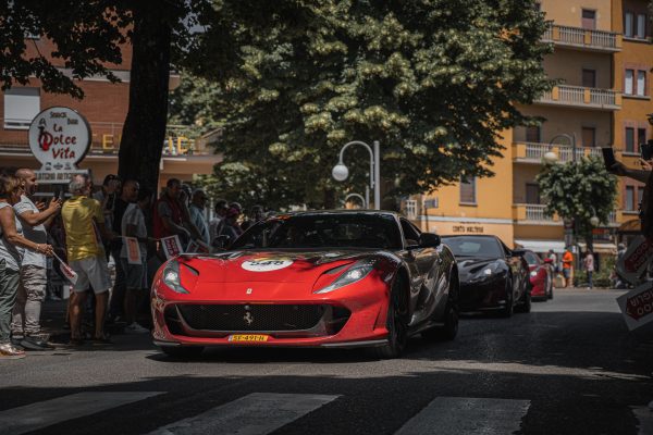 A vibrant street scene captures a red Ferrari amidst a bustling crowd during a city rally. Voitures 4K