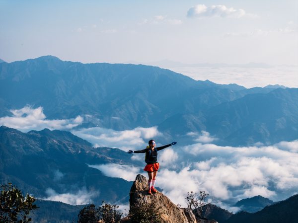 A woman celebrates atop a rocky peak surrounded by majestic mountain views and clouds. Nature 4K