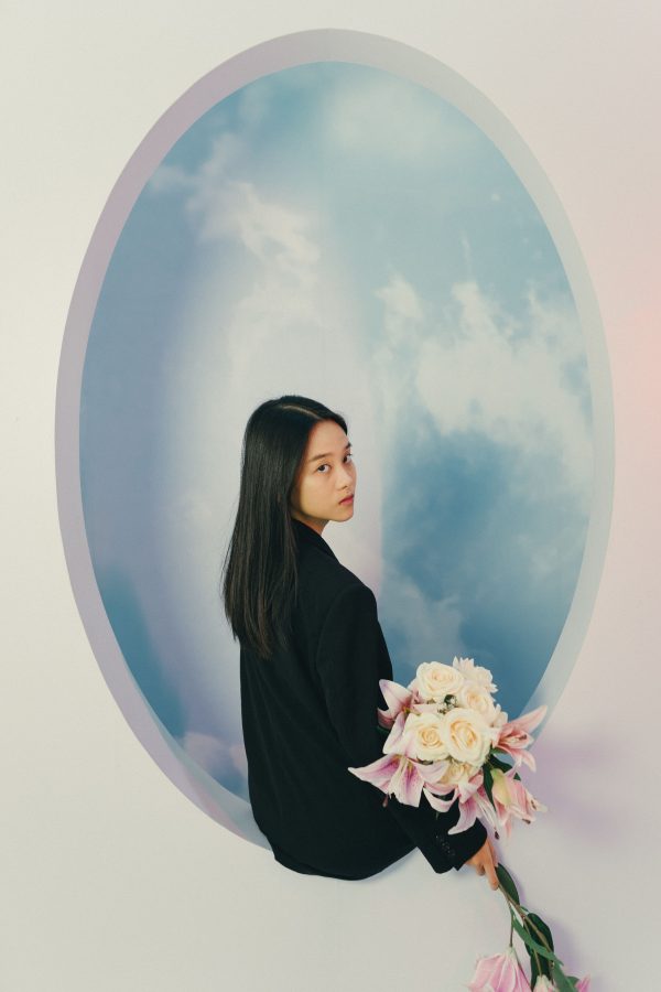 A woman holding flowers stands against a sky-themed backdrop, creating a dreamy artistic portrait. Mobile 4K