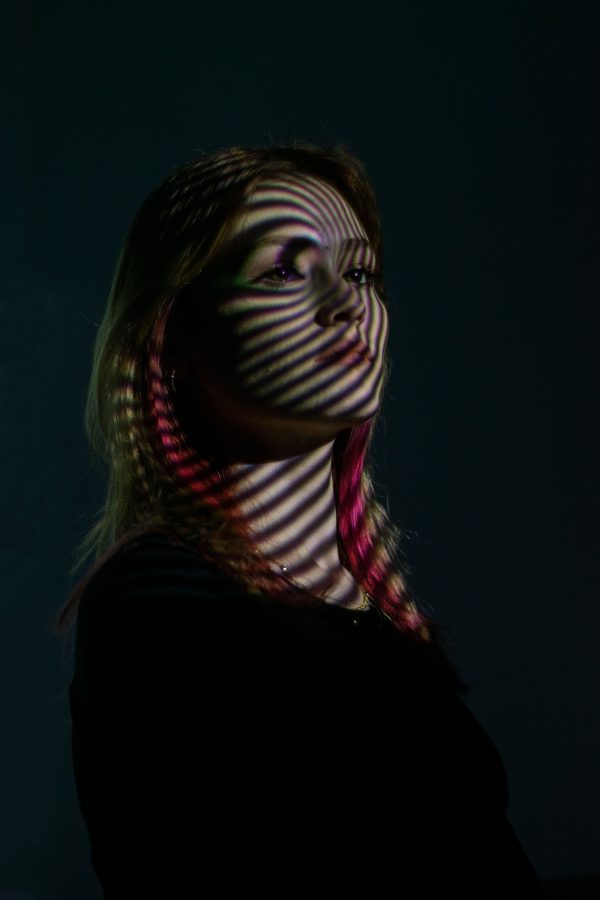 A woman in a dark setting with stripes of dramatic light creating an artistic shadow on her face. Mobile 4K