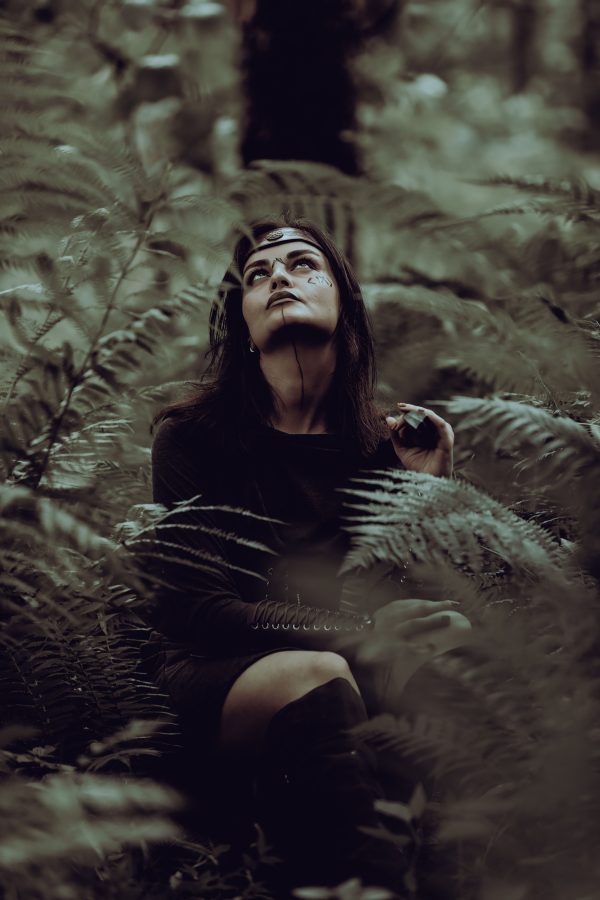 A woman in a mystical forest setting gazes upwards, surrounded by ferns and dark foliage. Mobile 4K