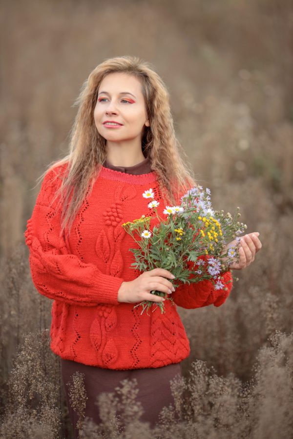 A woman in a red sweater stands outdoors holding a bouquet of colorful wildflowers. Mobile 4K