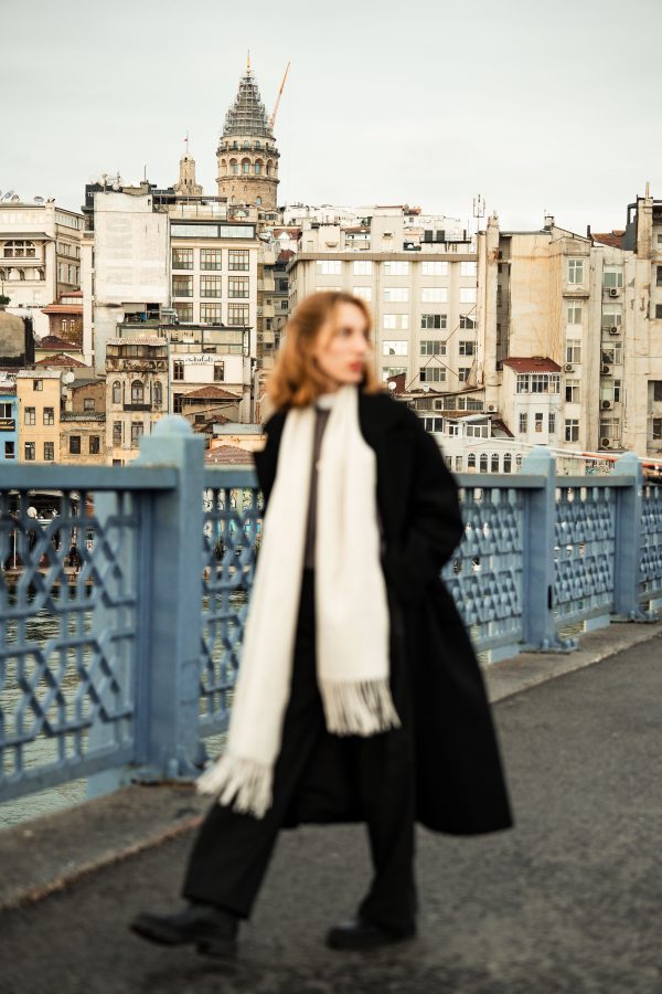 A woman in warm clothing walks on a bridge with a view of Istanbul's famous Galata Tower. Mobile 4K