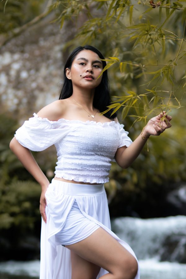 A woman in white attire poses gracefully in a lush green outdoor setting, surrounded by nature. Mobile 4K