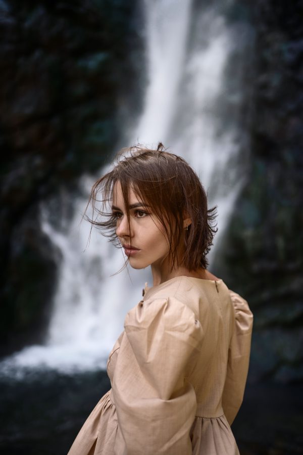 A woman stands elegantly before the stunning waterfall in Stepantsminda, Georgia, showcasing fashion and natural beauty. Mobile 4K