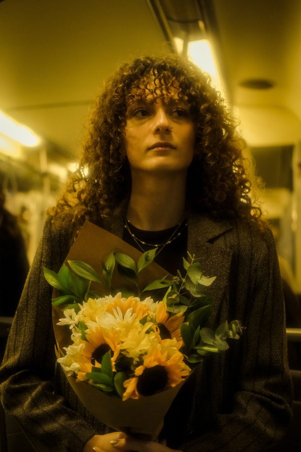A woman with curly hair holds a bouquet of sunflowers inside a train. Mobile 4K