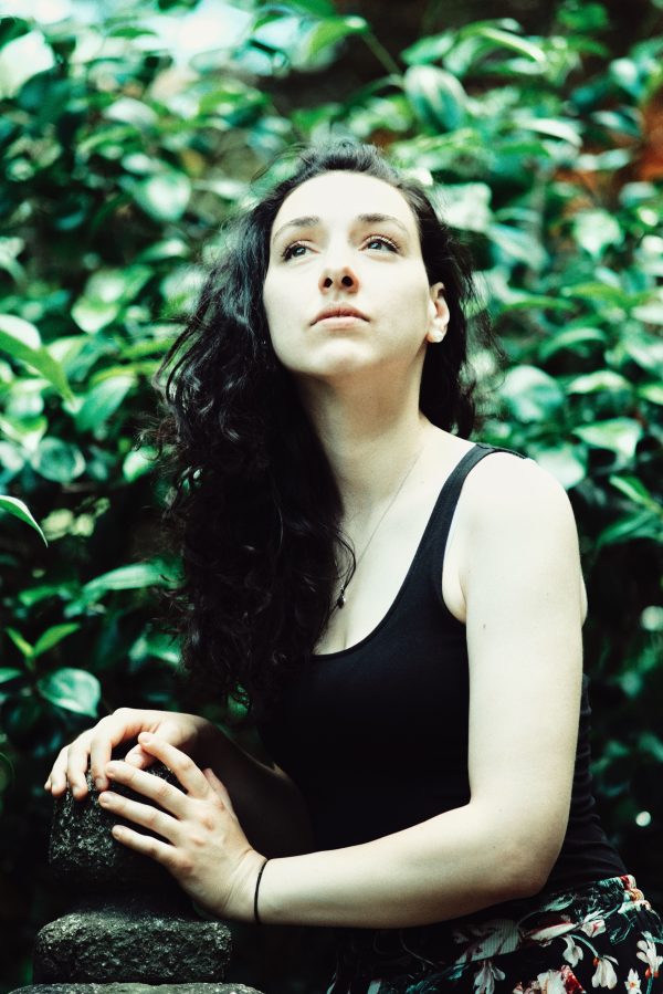 A woman with dark hair in a black tank top looks upward, surrounded by vibrant greenery. Mobile 4K