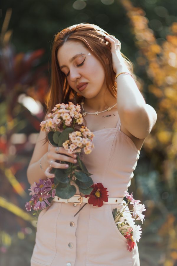 A young woman poses gracefully with flowers in a vibrant garden setting, showcasing a peaceful and serene moment. Mobile 4K