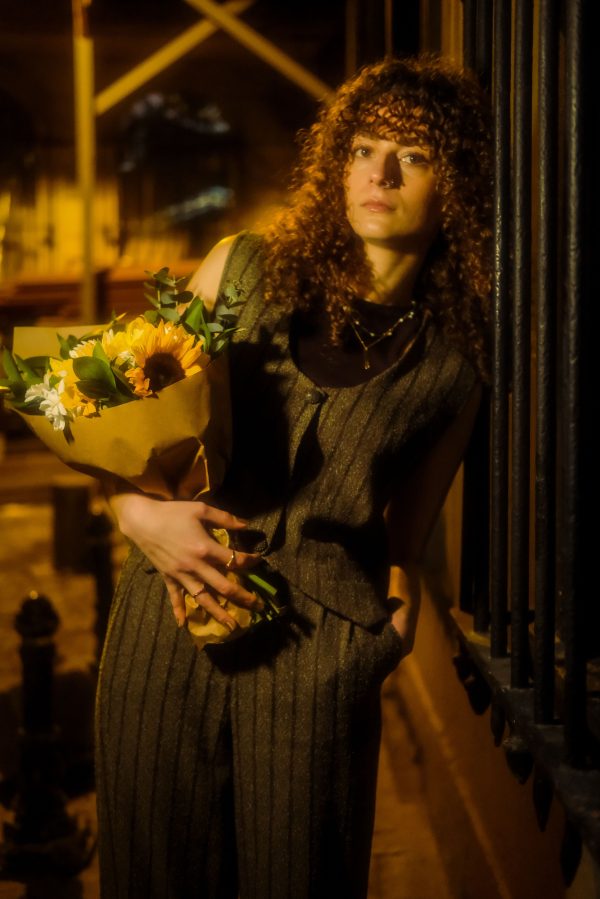 A young woman with curly hair holds a sunflower bouquet against an urban night backdrop. Mobile 4K