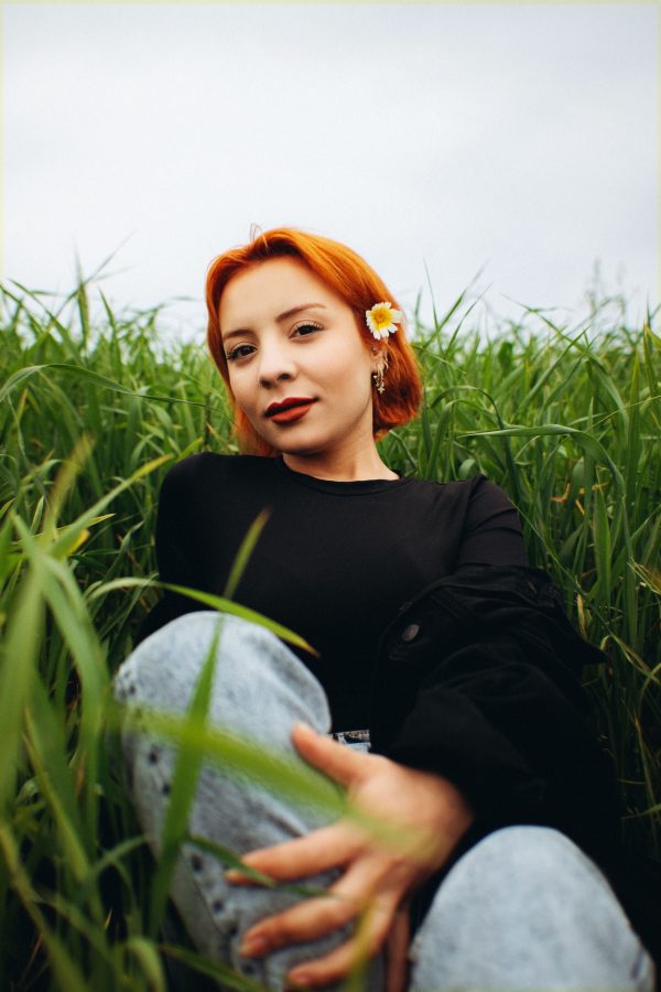 A young woman with red hair poses in a field, sporting a flower in her hair. Mobile 4K