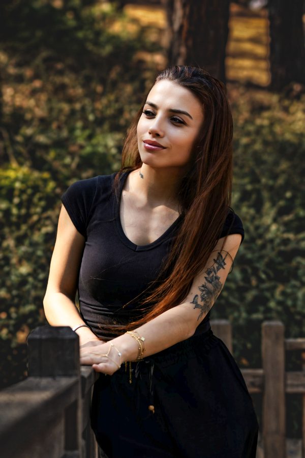 A young woman with tattoos leaning on a wooden rail, enjoying a sunny day outdoors. Mobile 4K