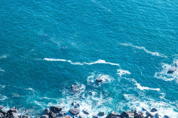 Aerial shot of clear blue ocean with waves crashing onto rocks along the coast. Nature 4K