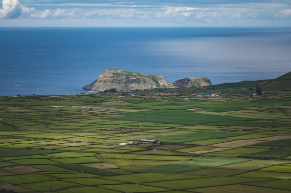 Aerial view of lush green farmland next to the ocean with distant island in the horizon. Nature 4K