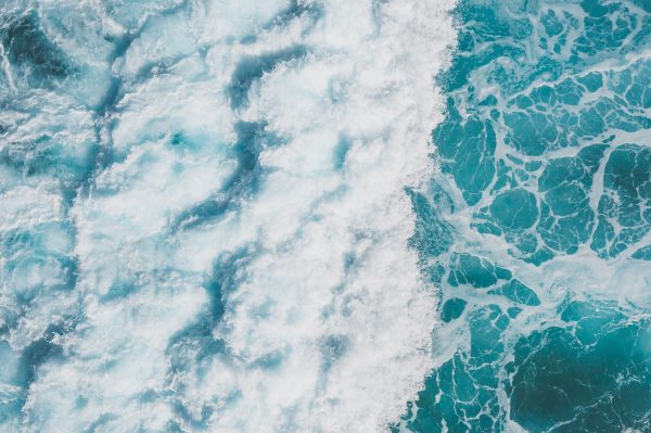 Aerial view of vibrant turquoise ocean waves creating white sea foam and splashes. Nature 4K