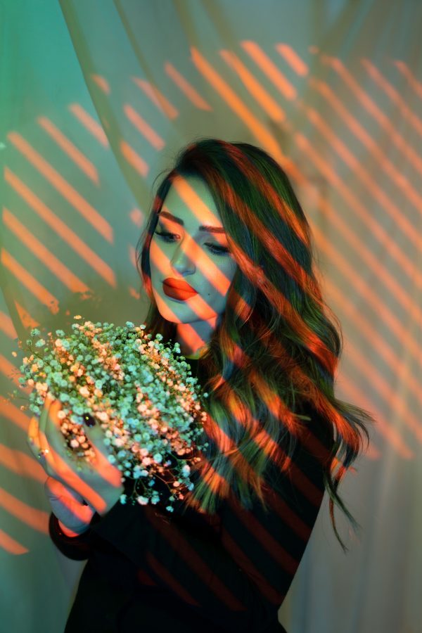 An artistic portrait of a woman holding a bouquet, illuminated by colorful striped lights, creating a dramatic effect. Mobile 4K