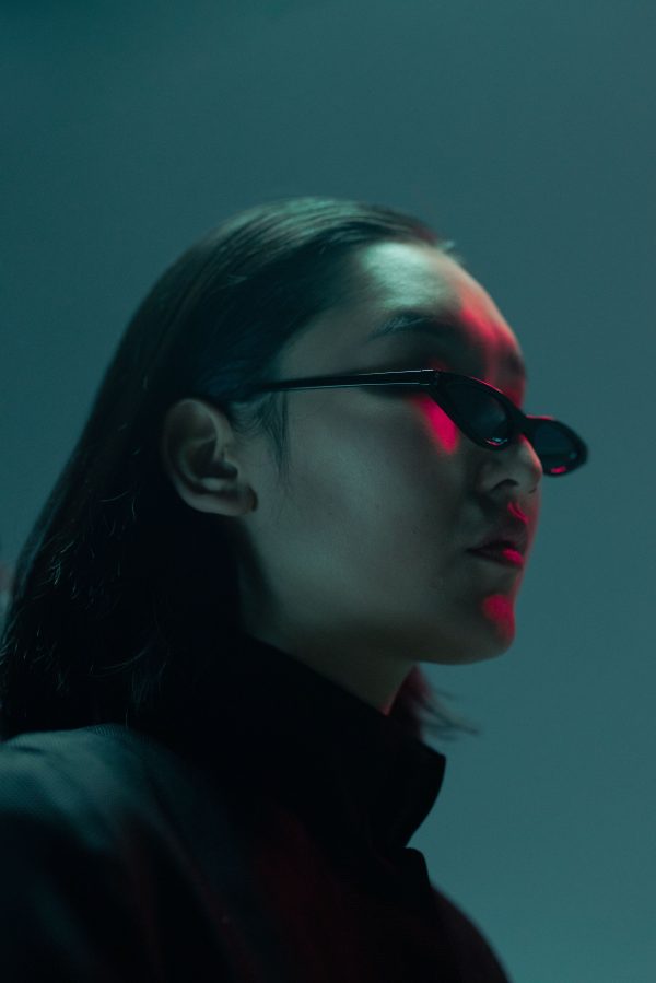 Artistic low-angle portrait of a woman with sunglasses in dramatic neon lighting. Mobile 4K