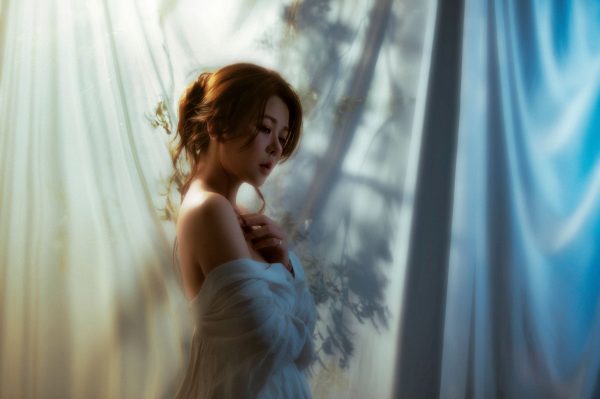 Artistic portrait of a woman in soft, dreamy lighting with shadows on a draped background. Charme 4K