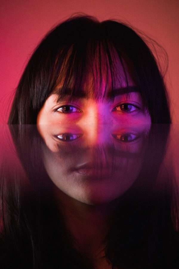 Artistic portrait of a woman using mirror reflection and pink lighting for a surreal effect. Mobile 4K