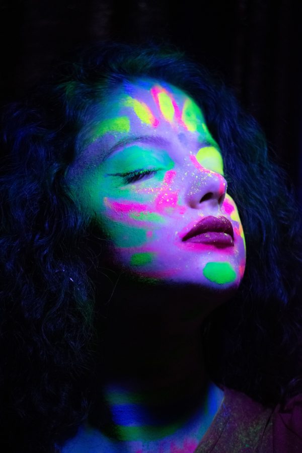 Artistic portrait of a woman with neon face paint glowing under UV light, eyes closed in serenity. Mobile 4K