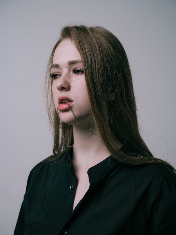 Artistic studio portrait of a young woman wearing a chain necklace and black shirt. Mobile 4K