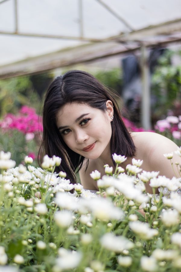 Beautiful Asian woman surrounded by vibrant white flowers in a garden setting. Mobile 4K