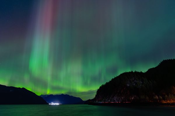 Beautiful display of Northern Lights over a serene mountain and water landscape at night. Espace 4K