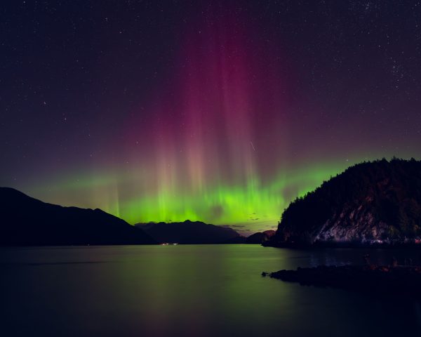 Beautiful northern lights reflecting over a calm lake with starry sky in the background. Espace 4K