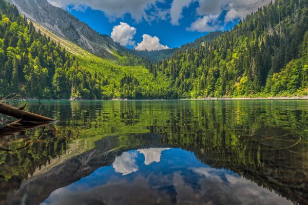 Beautiful reflection of lush mountains in a calm lake in Sochi, Russia, under a vibrant blue sky. Nature 4K